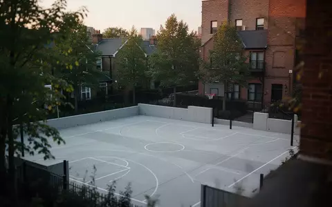Ein moderner, menschenleerer Sportplatz in einem Wohnviertel bei Dämmerung, umgeben von Bäumen und Architektur. - Foto: über boerse-global.de