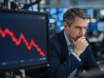 Ein besorgter Börsenhändler blickt auf einen Monitor mit einem fallenden Aktienkurs. - Foto: über boerse-global.de