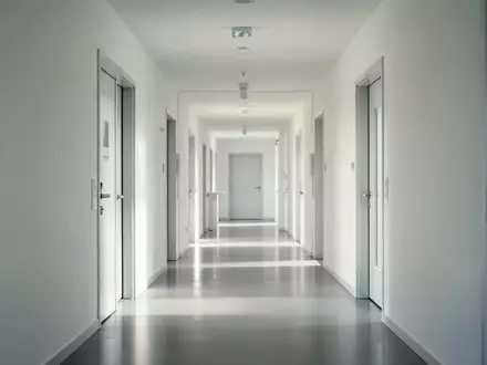 Ein minimalistischer, leerer Flur in einer modernen Schweizer Klinik mit hellem Tageslicht und sauberen, weißen Wänden. - Foto: über boerse-global.de