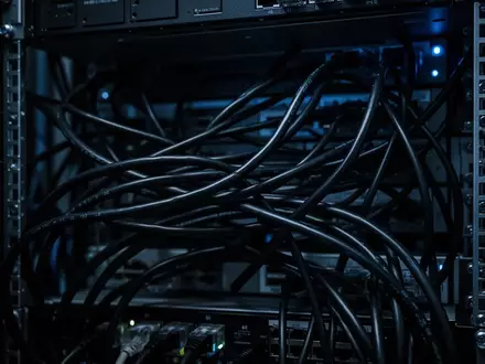 Dunkles, industrielles Serverrack mit unordentlichen schwarzen Kabeln und blauer Beleuchtung. - Foto: über boerse-global.de