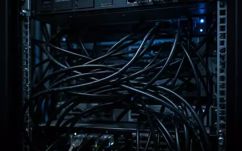 Dunkles, industrielles Serverrack mit unordentlichen schwarzen Kabeln und blauer Beleuchtung. - Foto: über boerse-global.de