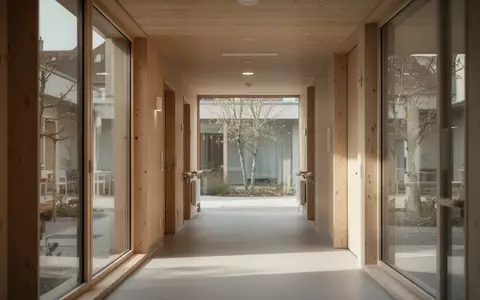 Ein ruhiger, von natürlichem Licht durchfluteter Flur in einem modernen Pflegeheim mit Blick auf einen begrünten Innenhof. - Foto: über boerse-global.de