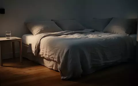 Ein minimalistisch eingerichtetes, ruhig wirkendes Schlafzimmer bei Dämmerlicht mit einem ordentlich gemachten Bett. - Foto: über boerse-global.de