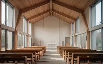 Innenraum einer modernen, schlichten Kirche mit Holzbänken und großen Fenstern bei natürlichem Tageslicht. - Foto: über boerse-global.de
