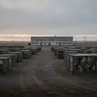 Ein weitläufiger, menschenleerer militärischer Übungsplatz in der Morgendämmerung mit schlichten Unterkunftsgebäuden. - Foto: über boerse-global.de