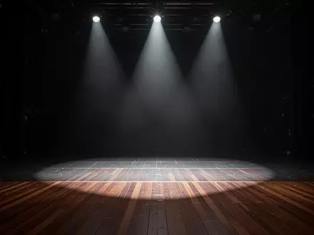 Eine menschenleere, professionelle Theaterbühne, die von dramatischen Lichtkegeln in einer dunklen Atmosphäre ausgeleuchtet wird. - Foto: über boerse-global.de