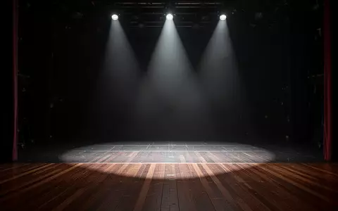 Eine menschenleere, professionelle Theaterbühne, die von dramatischen Lichtkegeln in einer dunklen Atmosphäre ausgeleuchtet wird. - Foto: über boerse-global.de