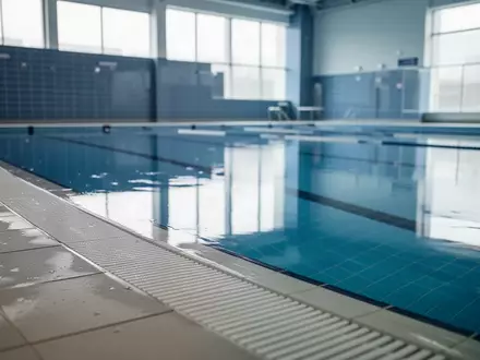 Ein ruhiges, leeres Schwimmbecken mit blauen Fliesen und spiegelnder Wasseroberfläche in einer hellen Schwimmhalle. - Foto: über boerse-global.de