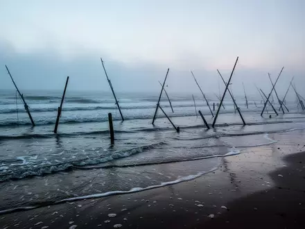 Eine neblige Nordseeküste mit Holzpfählen im Sand bei Sonnenaufgang. - Foto: über boerse-global.de