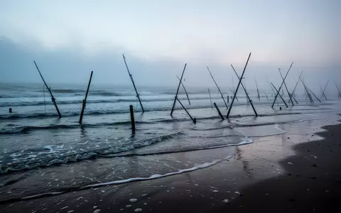 Eine neblige Nordseeküste mit Holzpfählen im Sand bei Sonnenaufgang. - Foto: über boerse-global.de
