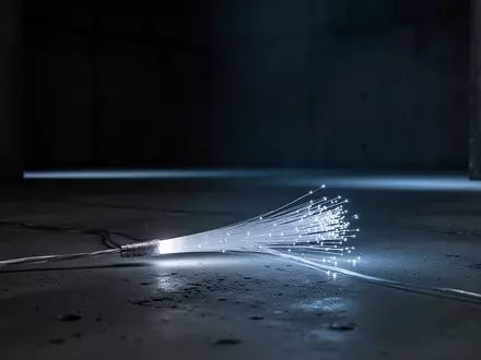 Ein einzelnes leuchtendes Glasfaserkabel auf einem dunklen, minimalistischen Betonuntergrund. - Foto: über boerse-global.de