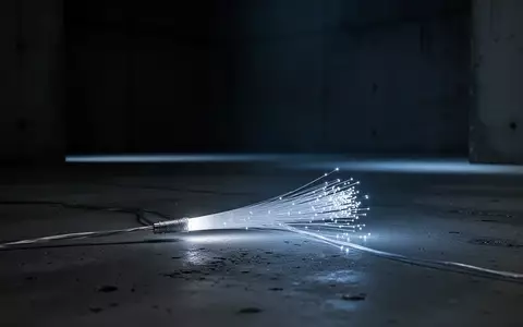 Ein einzelnes leuchtendes Glasfaserkabel auf einem dunklen, minimalistischen Betonuntergrund. - Foto: ĂŒber boerse-global.de
