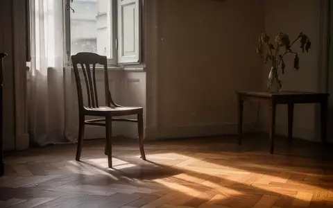 Ein leerer Holzstuhl in einem sonnendurchfluteten Raum mit einer Blumenvase auf einem Beistelltisch. - Foto: über boerse-global.de