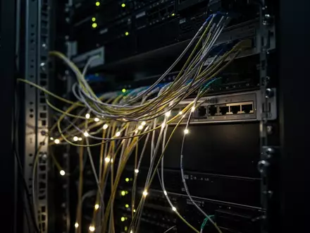 Nahaufnahme von Glasfaserkabeln in einem dunklen Serverraum zur Visualisierung von Netzwerksicherheit. - Foto: über boerse-global.de