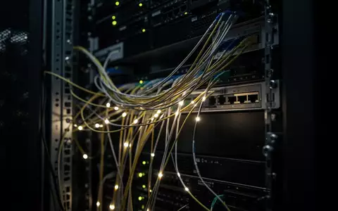 Nahaufnahme von Glasfaserkabeln in einem dunklen Serverraum zur Visualisierung von Netzwerksicherheit. - Foto: über boerse-global.de