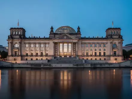 Das Reichstagsgebäude in Berlin in der Dämmerung, aufgenommen von der Spree aus mit Fokus auf die Architektur. - Foto: über boerse-global.de