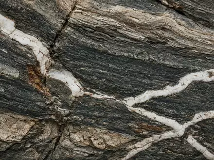 Nahaufnahme einer geologischen Gesteinsformation mit markanten mineralischen Adern in einem Amphibolit-Gestein. - Foto: über boerse-global.de