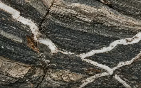 Nahaufnahme einer geologischen Gesteinsformation mit markanten mineralischen Adern in einem Amphibolit-Gestein. - Foto: über boerse-global.de