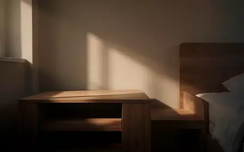 Ein schlichtes, ruhig wirkendes Schlafzimmer mit einem leeren Nachttisch im gedämpften Morgenlicht. - Foto: über boerse-global.de