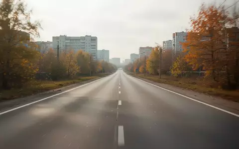 Eine leere Asphaltstraße, die sich durch eine herbstliche Stadtlandschaft erstreckt. - Foto: über boerse-global.de