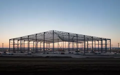 Skelett eines großen Industriebaus auf einer weiten Baustelle bei Dämmerung als Symbol für Infrastrukturentwicklung. - Foto: über boerse-global.de