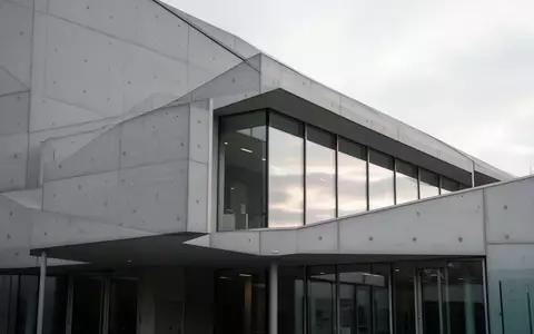Moderne Architektur eines Verwaltungsgebäudes mit grauen Betonwänden und Glasfronten bei Tageslicht. - Foto: über boerse-global.de