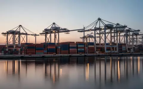 Moderne Containerterminals in einem Hafen mit gestapelten Containern und Portalkränen bei Dämmerung. - Foto: über boerse-global.de