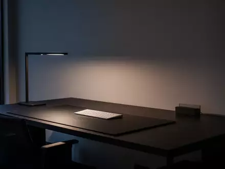 Ein minimalistisch gestalteter, aufgeräumter Schreibtisch in einem modernen Büro bei Dämmerung mit atmosphärischer Beleuchtung. - Foto: über boerse-global.de