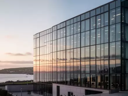 Modernes Bürogebäude vor einer Küstenlandschaft auf der Isle of Man bei Sonnenuntergang. - Foto: über boerse-global.de