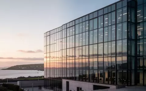 Modernes Bürogebäude vor einer Küstenlandschaft auf der Isle of Man bei Sonnenuntergang. - Foto: über boerse-global.de