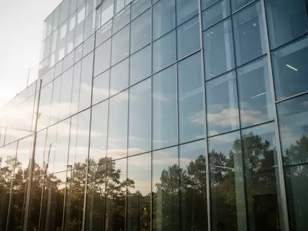 Große, sonnendurchflutete Glasfassade eines modernen Gebäudes mit klaren Spiegelungen des Himmels und der Umgebung. - Foto: über boerse-global.de