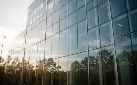 Große, sonnendurchflutete Glasfassade eines modernen Gebäudes mit klaren Spiegelungen des Himmels und der Umgebung. - Foto: über boerse-global.de