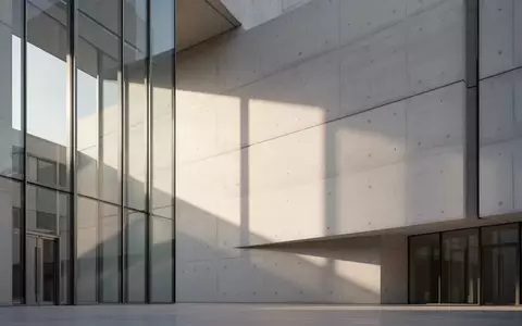 Eine moderne, minimalistische Fassade eines öffentlichen Gebäudes mit geometrischen Schattenwürfen bei Morgenlicht. - Foto: über boerse-global.de