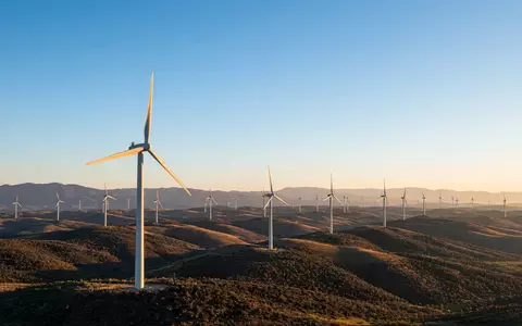 Moderne Windkraftanlagen in einer weitläufigen Landschaft bei Sonnenuntergang. - Foto: über boerse-global.de