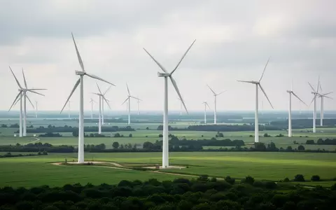 Moderne Windkraftanlagen in einer grünen Landschaft unter einem bewölkten Himmel. - Foto: über boerse-global.de