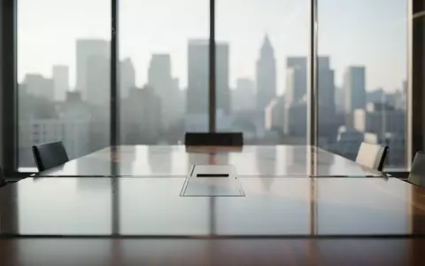 Moderner, leerer Konferenzraum mit Glaswänden und Blick auf eine verschwommene Stadt bei Tageslicht. - Foto: über boerse-global.de