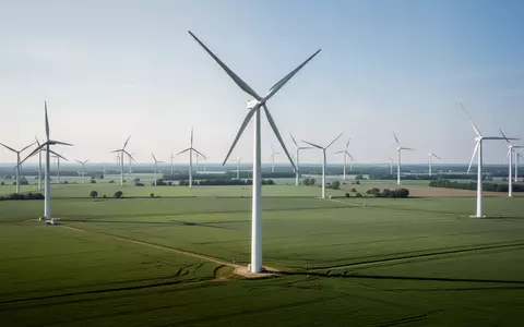 Moderne Windkraftanlagen in einer weiten grünen Landschaft unter einem klaren Himmel. - Foto: über boerse-global.de