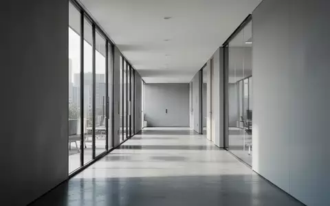 Ein minimalistischer, leerer Büroflur mit polierten Betonböden und hellem Tageslicht, das durch große Fenster einfällt. - Foto: über boerse-global.de