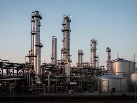 Weite Ansicht einer weitläufigen Chemieanlage mit Edelstahltürmen und Rohrleitungssystemen bei Dämmerung. - Foto: über boerse-global.de