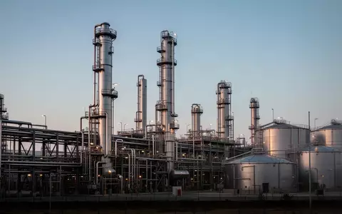 Weite Ansicht einer weitläufigen Chemieanlage mit Edelstahltürmen und Rohrleitungssystemen bei Dämmerung. - Foto: über boerse-global.de