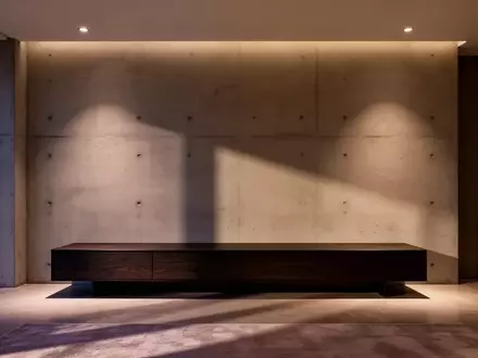 Ein minimalistisch gestaltetes, modernes Wohnzimmer mit einer dunklen Medienkonsole vor einer Betonwand bei Dämmerung. - Foto: über boerse-global.de