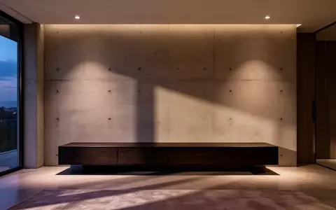 Ein minimalistisch gestaltetes, modernes Wohnzimmer mit einer dunklen Medienkonsole vor einer Betonwand bei Dämmerung. - Foto: über boerse-global.de