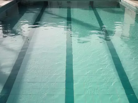 Blick von oben in eine leere, türkisblaue Schwimmbahn mit klarem Wasser und reflektierendem Licht auf dem Boden. - Foto: über boerse-global.de