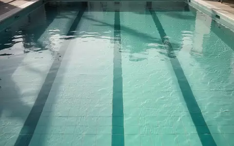 Blick von oben in eine leere, türkisblaue Schwimmbahn mit klarem Wasser und reflektierendem Licht auf dem Boden. - Foto: über boerse-global.de