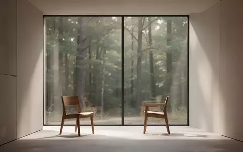 Ein minimalistisch eingerichteter, sonnendurchfluteter Raum mit einem leeren Stuhl vor einem Fenster mit Blick auf einen Wald. - Foto: über boerse-global.de