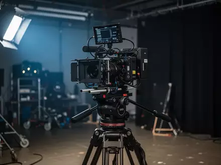 Professionelle Filmkamera auf einem Stativ in einem abgedunkelten Filmstudio mit Kinobeleuchtung. - Foto: über boerse-global.de