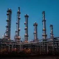Eine industrielle Ölraffinerie bei Dämmerung mit hohen Destillationstürmen und Rohrleitungen vor einem blauen Himmel. - Foto: über boerse-global.de