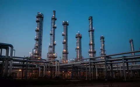 Eine industrielle Ölraffinerie bei Dämmerung mit hohen Destillationstürmen und Rohrleitungen vor einem blauen Himmel. - Foto: über boerse-global.de