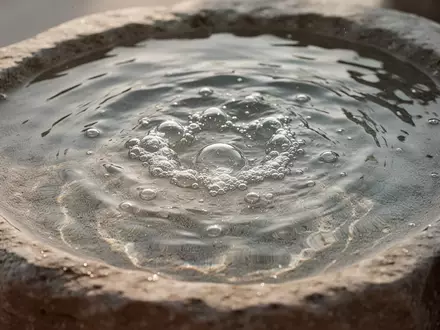 Nahaufnahme einer klaren Wasseroberfläche in einem Natursteinbecken mit sanften Lichtreflexionen. - Foto: über boerse-global.de