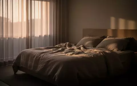 Ein minimalistisch eingerichtetes Schlafzimmer in den frühen Morgenstunden mit sanftem Licht und ungemachtem Bett. - Foto: über boerse-global.de